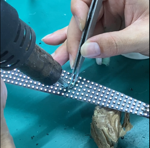 Engineer repairing pixel lamp on custom-shaped LED module with hot air gun and testing flexibility – high grayscale seamless LED display repair.